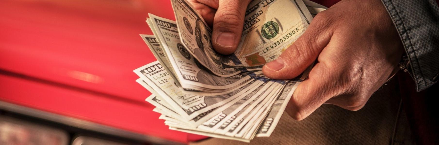 Man fanning out cash with a red car in the background