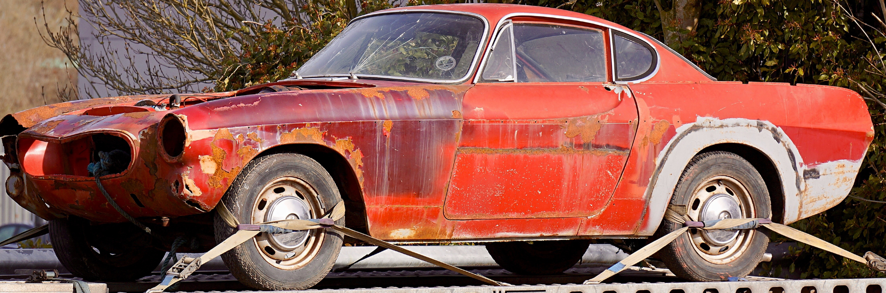 rusted, dilapidated junk car sitting in salvage yard 