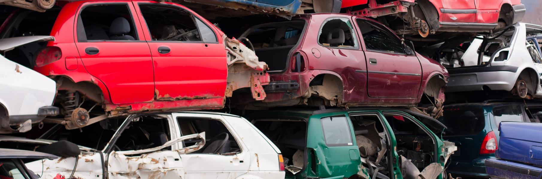 Multiple colored junk cars shown stacked together in a junkyard.