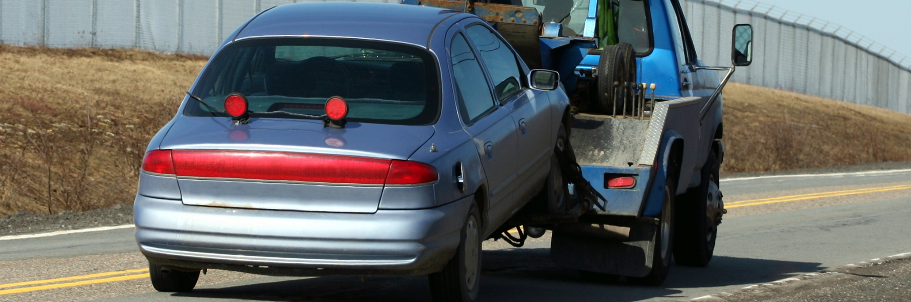 Silver car being hauled by a blue tow-truck down the road